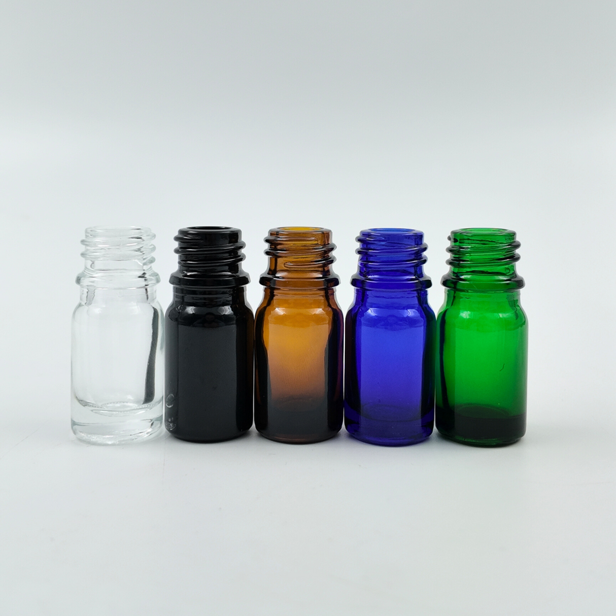 Set of 5ml glass bottles in clear, black, amber, blue, and green arranged side by side on a white background.