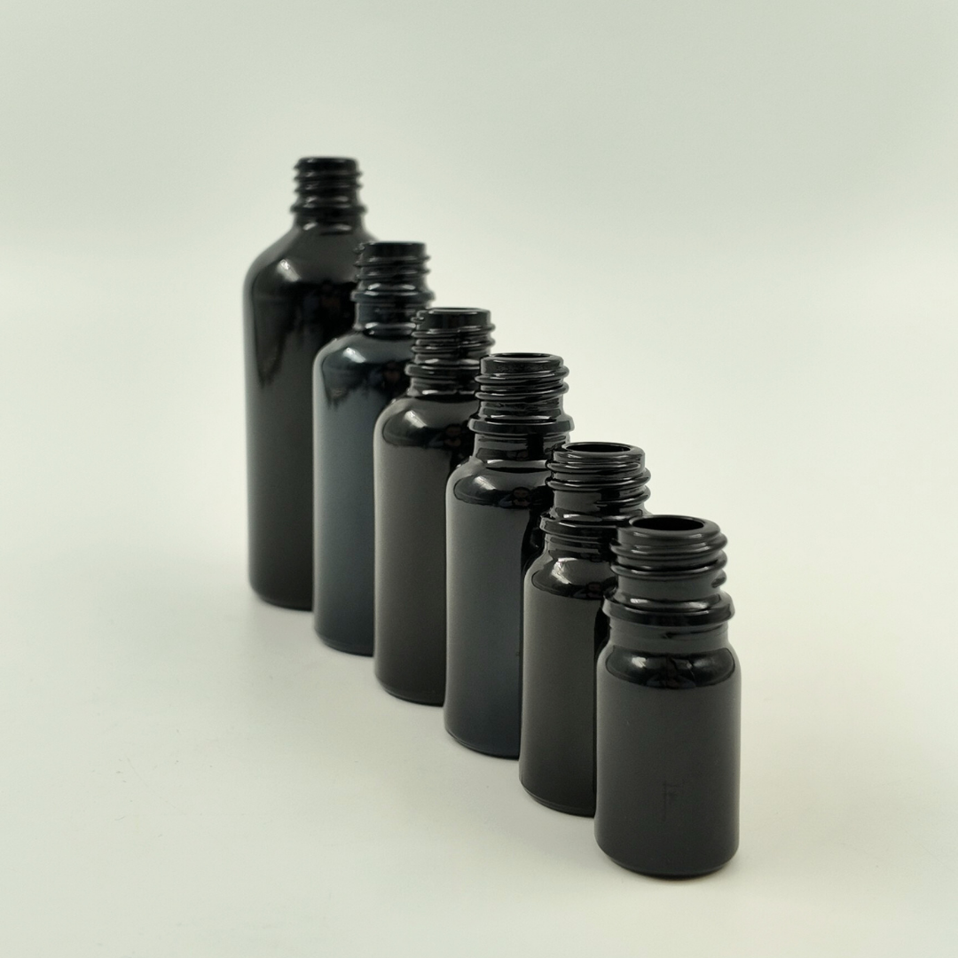 Lifestyle image of black glass bottles in different sizes arranged on a surface