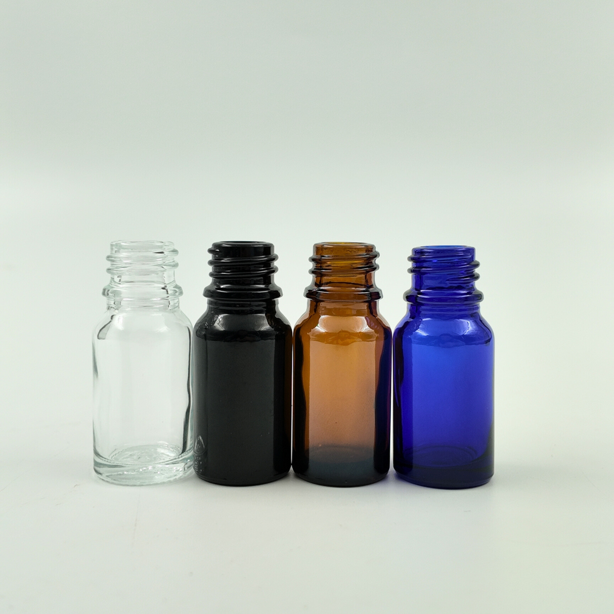 Set of 10ml glass dropper bottles in clear, amber, blue, and black arranged side by side on a white background.
